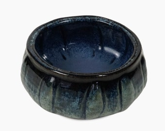 May include: A small, dark blue ceramic bowl with a textured, rippled exterior. The bowl has a smooth, glossy interior.