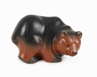 May include: A ceramic bear figurine with a black and brown glaze. The bear is in a crouching position with its head down.