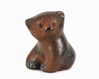 May include: A small ceramic bear figurine with brown and black glaze. The bear has a cute, cartoon-like face with black eyes and a black nose.