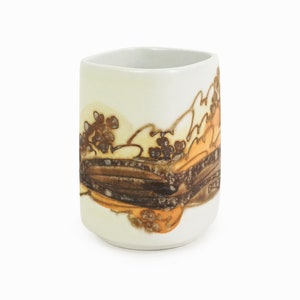 Può includere: Una tazza in ceramica bianca con un design unico. La tazza presenta un motivo astratto marrone e arancione su uno sfondo color crema. La tazza ha una forma quadrata e una finitura liscia e lucida.