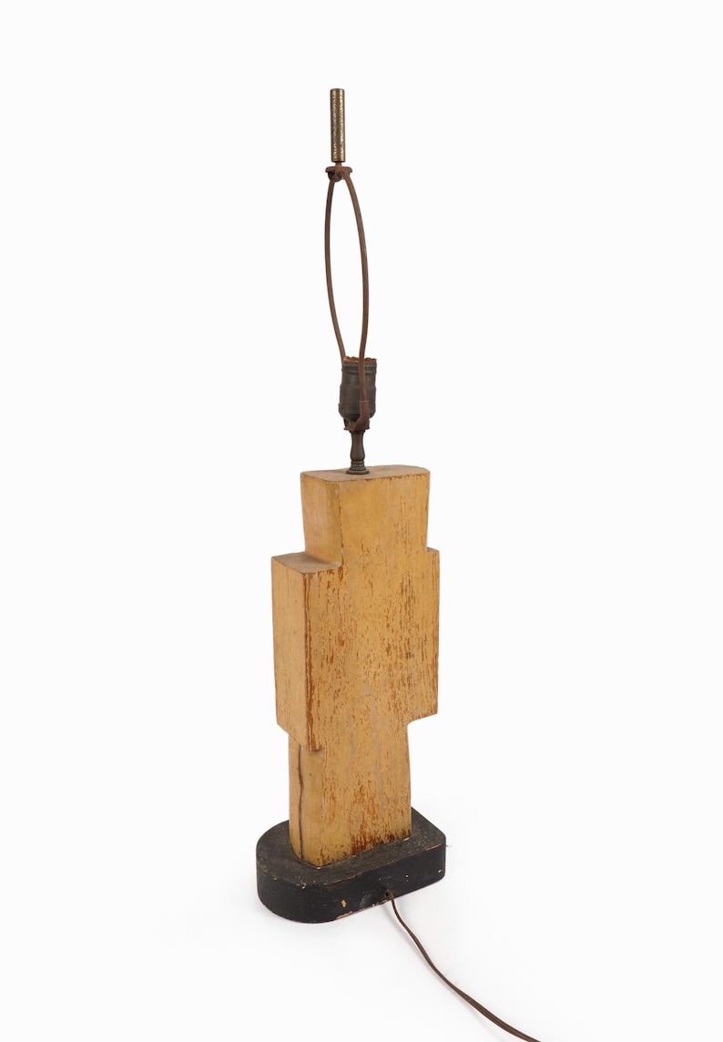 May include: A unique, geometric table lamp with a light brown, textured wooden body. The lamp has a black base and a brown cord. The lamp's height is approximately 20 inches.