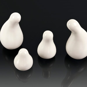 May include: Four white ceramic figurines shaped like pears, each with a unique, slightly different shape. The figurines are arranged in a row on a black surface.