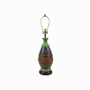 May include: A green ceramic table lamp with a brown, orange, and blue geometric pattern. The lamp has a simple, round base and a metal shade.