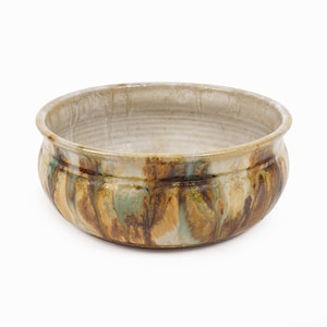 May include: A handcrafted ceramic bowl with a wide, shallow design. The bowl features a beige interior and a textured exterior with streaks of brown, green, and tan. The rim is slightly flared, and the bowl sits on a white background.