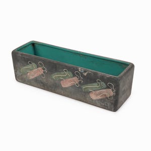 以下が含まれることがあります： 濃いグレーの外側とターコイズブルーの内側を持つ長方形のプランター。プランターは、緑、ピンク、白の抽象的な形状の繰り返しデザインが特徴です。植物用の装飾的な容器。