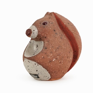 May include: A brown ceramic squirrel figurine with white and red accents. The squirrel has a speckled brown glaze and a red stripe down its back. The figurine is signed "McIlroy" on the bottom.
