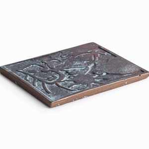 May include: A rectangular bronze plaque with a raised design of stylized leaves and flowers. The plaque has a greenish patina.