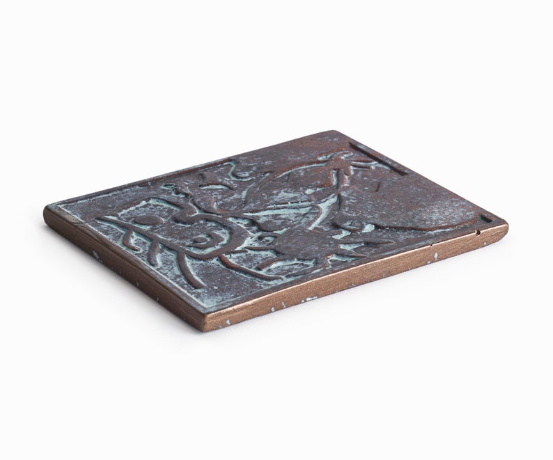 May include: A rectangular bronze plaque with a raised design of stylized leaves and flowers. The plaque has a greenish patina.