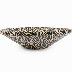 May include: A large, black and white zebra-print serving bowl made of wood. The bowl is wide and shallow, with a slightly flared rim.