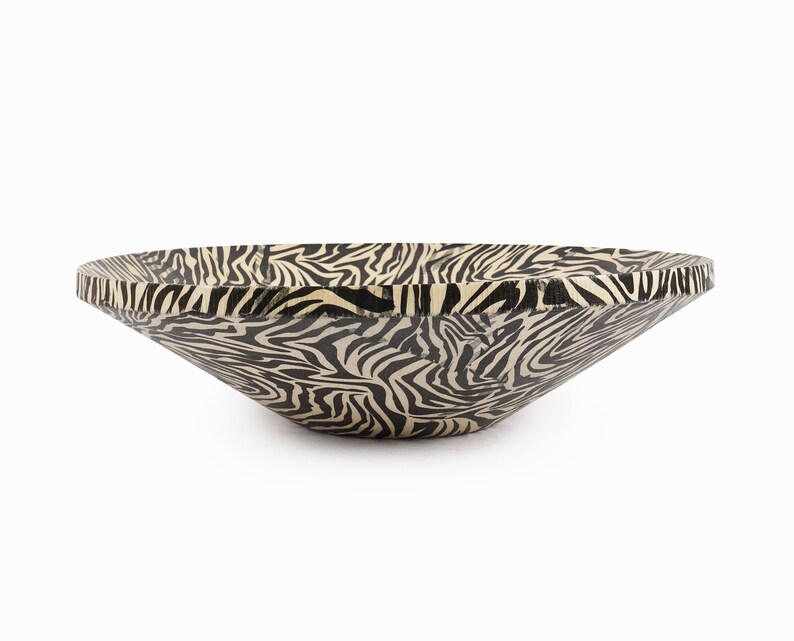 May include: A large, black and white zebra-print serving bowl made of wood. The bowl is wide and shallow, with a slightly flared rim.
