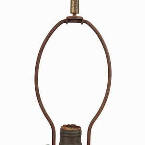 May include: A vintage lamp harp with a rusty brown finish. The lamp harp has a metal frame with a bulb socket and a decorative finial. The lamp harp is designed to hold a lampshade and is suitable for a table lamp.