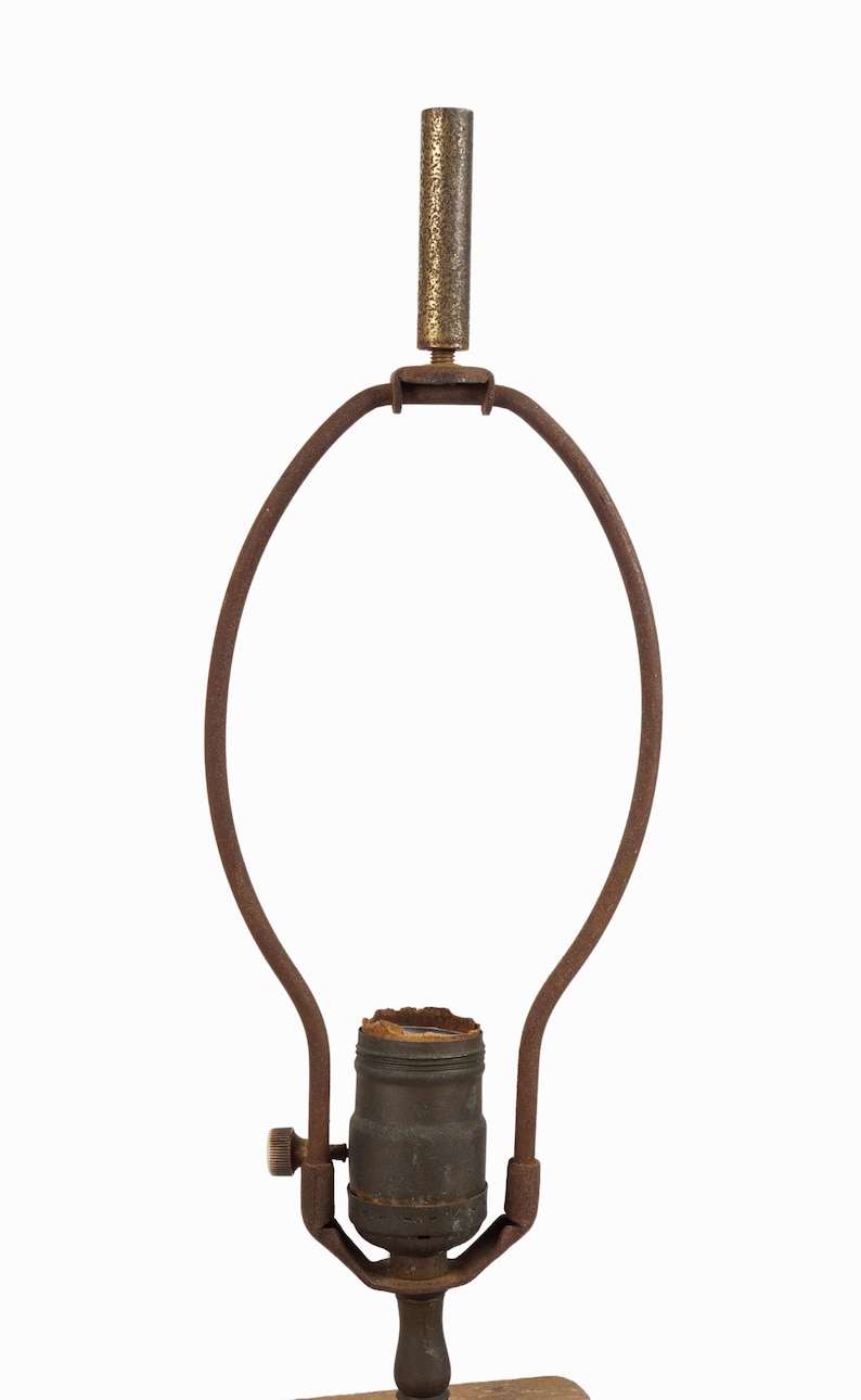 May include: A vintage lamp harp with a rusty brown finish. The lamp harp has a metal frame with a bulb socket and a decorative finial. The lamp harp is designed to hold a lampshade and is suitable for a table lamp.