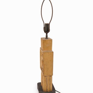May include: A vintage wooden lamp with a light brown finish. The lamp has a rectangular base and a carved design on the body. The lamp has a metal lamp holder and a brown electrical cord.