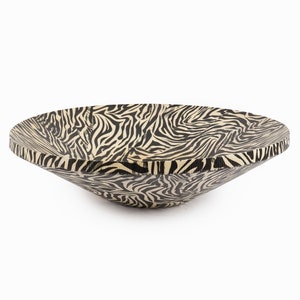 May include: A large, shallow bowl with a black and white zebra print design. The bowl is made of wood and has a rounded shape.