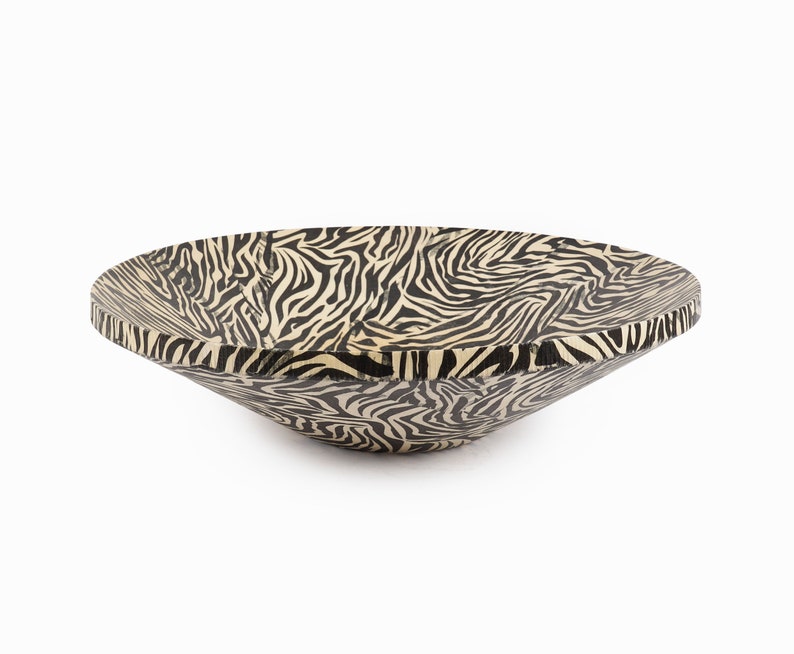 May include: A large, shallow bowl with a black and white zebra print design. The bowl is made of wood and has a rounded shape.
