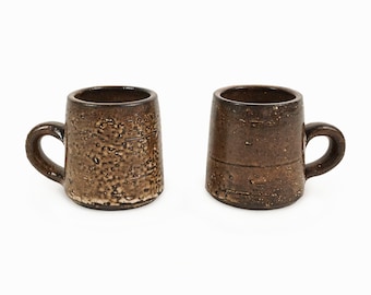May include: Two brown ceramic mugs with a textured surface. The mugs have a rounded shape and a handle.