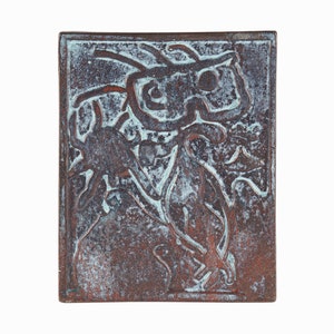 May include: A square ceramic tile with a raised design of a stylized creature in a copper and blue glaze.