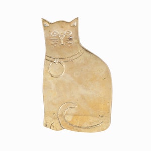 Puede incluir: Una figurita de gato de metal de color dorado con un collar y una etiqueta. El gato está sentado con la cola enroscada alrededor de sus patas.