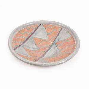 May include: A ceramic bowl with a light gray glaze and a geometric design. The design features three white triangles with a pink and green wavy pattern in the background.