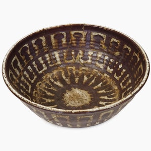 Puede incluir: Un cuenco de cerámica marrón con un diseño geométrico blanco. El cuenco tiene un borde ancho y un fondo redondeado.