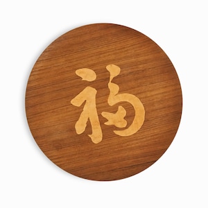 May include: A round wooden coaster with a light brown wood grain. The coaster has a light brown Chinese character "福" (Fu) meaning "good fortune" or "happiness" carved into the surface.