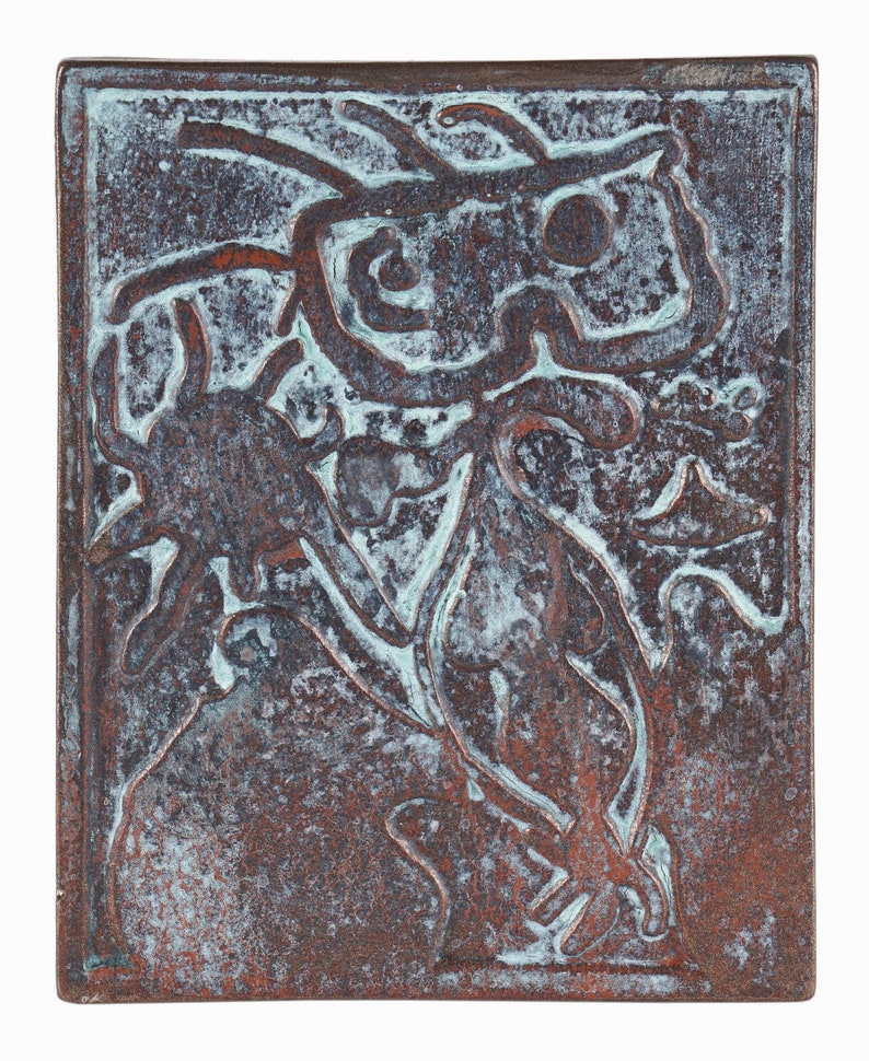 May include: A copper-colored ceramic tile with a raised design of a stylized figure. The figure is outlined in a lighter shade of copper and has a textured surface.