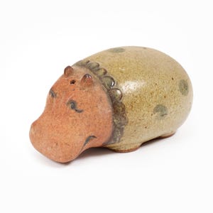 May include: A ceramic hippo figurine with a brown head and a light green body with dark green spots. The hippo has small black eyes and a decorative collar. The figurine is a unique home decor item.