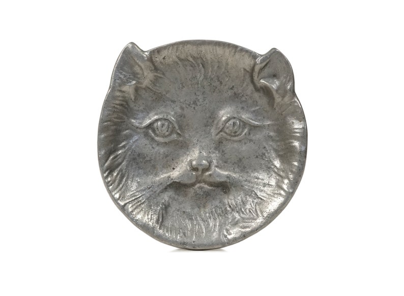 Puede incluir: Un plato de metal plateado con forma de cara de gato. El plato tiene un dise&ntilde;o detallado de la piel y las caracter&iacute;sticas de un gato.