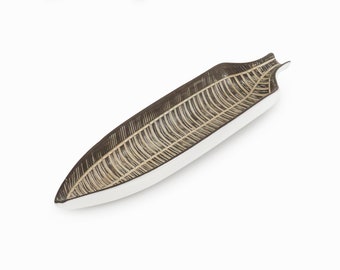 Könnte beinhalten: Eine lange, schmale Servierplatte aus Keramik mit weißem Innenraum und braunem Außenraum. Die Platte ist mit einem Muster aus Linien verziert, die einem Blatt ähneln.