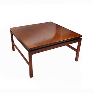 May include: A square, wooden coffee table with a dark brown finish. The table has a simple, mid-century modern design with a rectangular top and four legs.
