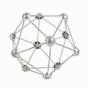 Pode incluir: Uma escultura de metal prateado com um design geométrico. A escultura é composta por uma série de esferas e hastes conectadas, criando uma forma tridimensional.