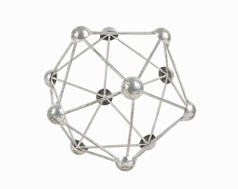 Könnte beinhalten: Eine silberne Metallskulptur mit geometrischem Design. Die Skulptur besteht aus einer Reihe von verbundenen Kugeln und Stäben, die eine dreidimensionale Form bilden.