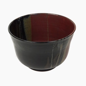 May include: A black ceramic bowl with red, yellow, and brown stripes. The bowl is glazed and has a smooth finish.