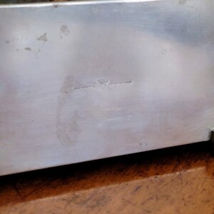 May include: Silver metal box with a glass top. The box has a small inscription on the bottom that reads "Made in England".