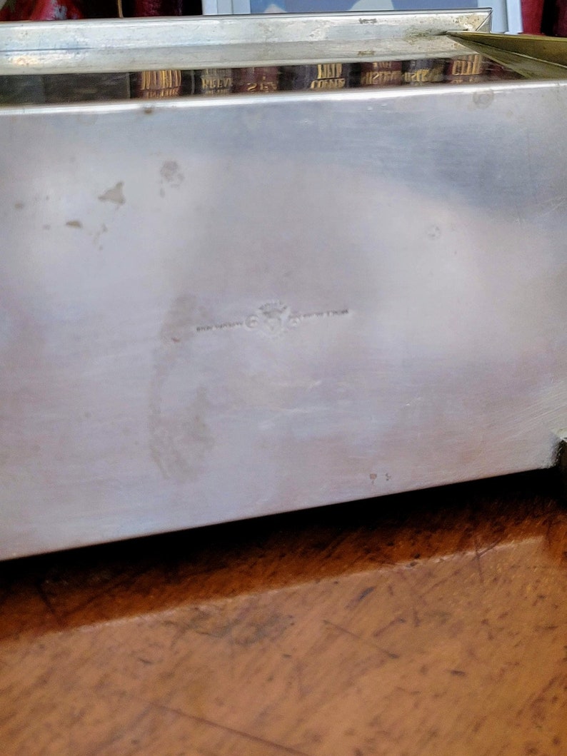 May include: Silver metal box with a glass top. The box has a small inscription on the bottom that reads "Made in England".