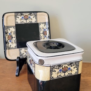 May include: A vintage ceramic serving set comprising a square lidded container and a rectangular tray. The set features a black and cream colour scheme with floral and scrollwork designs. The container has a black lid and a cream-coloured rim.