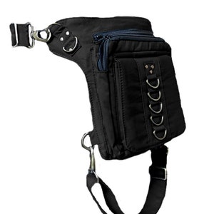 May include: Black canvas thigh bag with multiple pockets and a strap that goes around the leg. The bag has a zipper closure and metal accents.