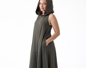 May include: Olive green hooded maxi dress. Sleeveless design with a relaxed fit and pockets. The dress features a hood and a flowing skirt. The model is wearing the dress. The dress is made of a soft, flowing fabric.