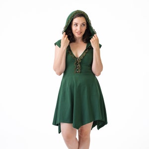 Puede incluir: Una mujer con un vestido verde con capucha y ribete de encaje y botas marrones. El vestido tiene un escote en V y un cierre de botón.