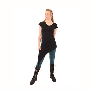 May include: A black asymmetrical tunic top with short sleeves and a V-neckline. The model is wearing the top with teal leggings and black boots.