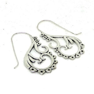 May include: A pair of silver dangle earrings with a delicate, intricate design. The earrings are made of metal and have a filigree pattern.