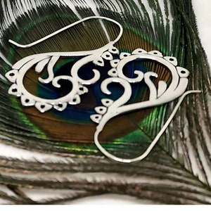 May include: A pair of silver filigree earrings with a delicate, intricate design. The earrings are shown on a peacock feather background.
