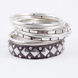 May include: A stack of silver bangles with a black and silver studded bangle on the bottom.