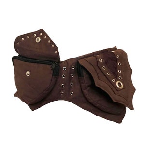 May include: A brown canvas fanny pack with multiple pockets and metal eyelets. The pack has a zipper closure and a flap with a metal ring.