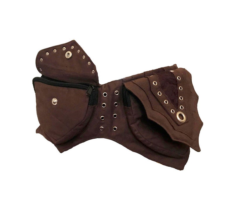 May include: A brown canvas fanny pack with multiple pockets and metal eyelets. The pack has a zipper closure and a flap with a metal ring.