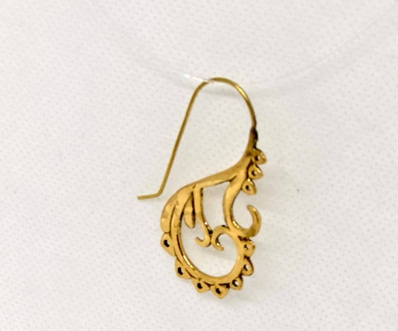 May include: A gold-colored earring with a delicate, intricate design. The earring is shaped like a stylized flower or leaf, with a curved, openwork pattern.