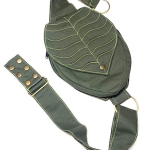 May include: A green canvas crossbody bag with a leaf design. The bag has a long adjustable strap and a metal buckle. The leaf design is stitched with a yellow thread.