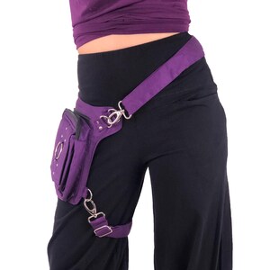 May include: Purple fanny pack with a silver buckle and chain. The pack is worn on the hip and has a strap that goes over the shoulder.