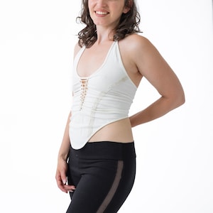 May include: A woman wearing a white halter top with a lace design and black leggings with a mesh panel on the side.