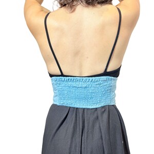 May include: A black top with thin straps and a light blue, smocked bandeau-style top. The bottom portion of the outfit is a dark gray, flowing skirt. The outfit is shown from the back.